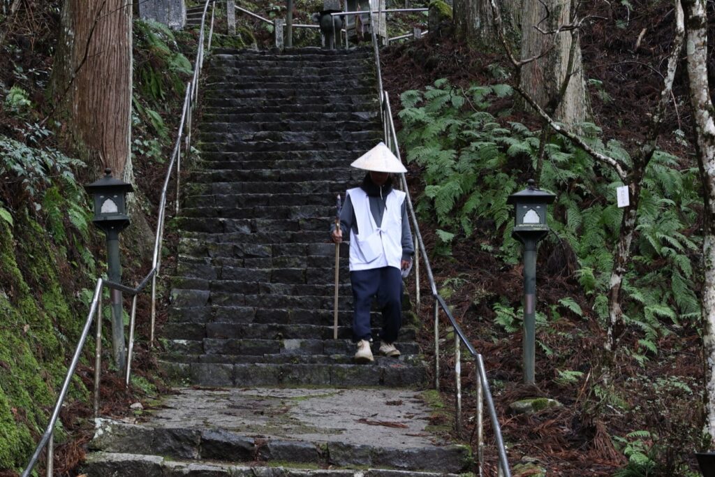 A pilgrim in traditional garb descends the stone staircase at Iwaya-ji, Pilgrimage Temple 45.