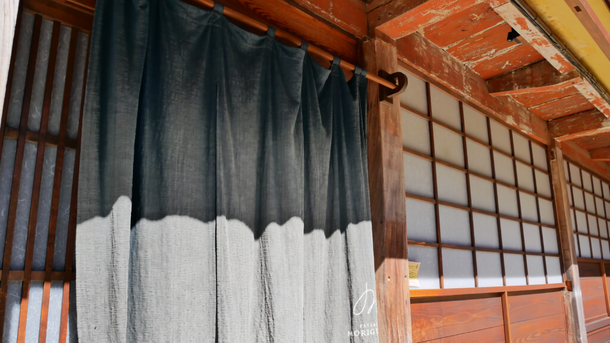 A traditional noren curtain with the logo of PAYSAGE MORIGUCHI hanging at the entrance of the renovated historical boutique hotel.