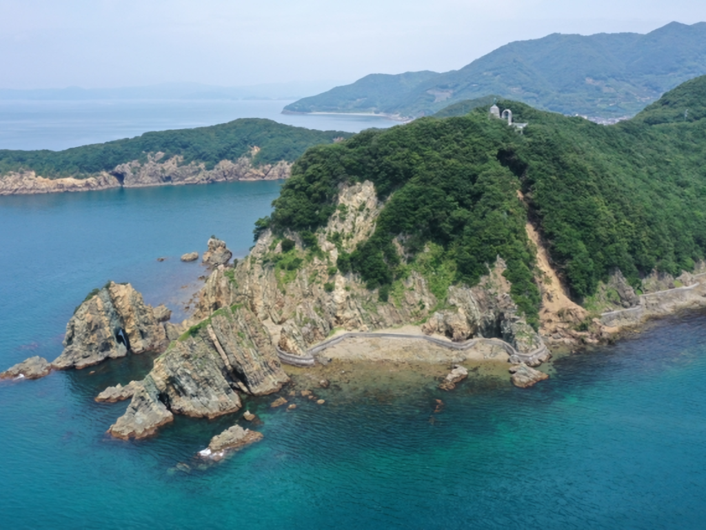 Suzaki Coast in Seiyo City, Ehime Prefecture. A panoramic view of a lush green cape and cliffs with complex geological strata jutting into the blue sea.