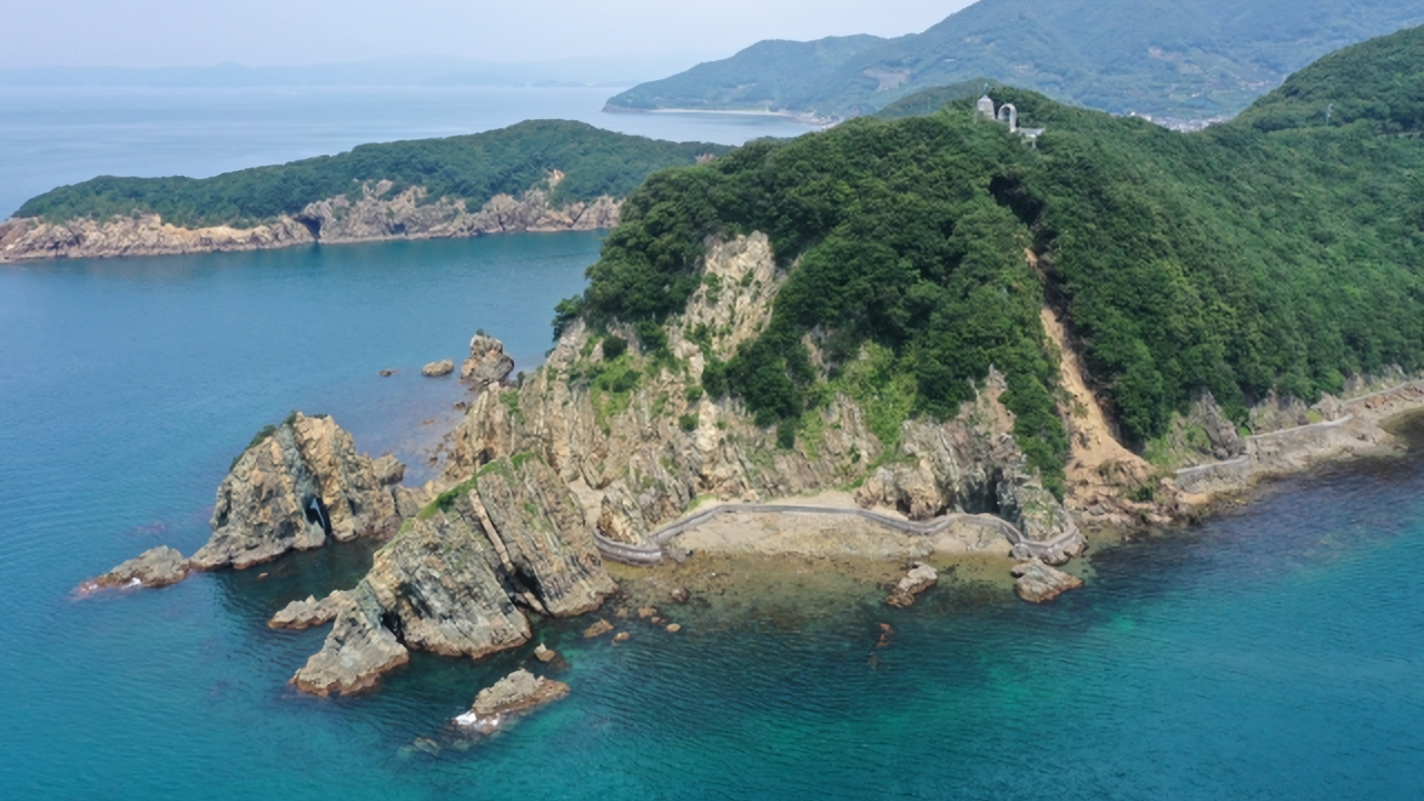 Suzaki Coast in Seiyo City, Ehime Prefecture. A panoramic view of a lush green cape and cliffs with complex geological strata jutting into the blue sea.