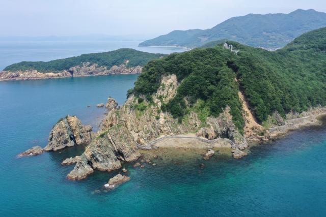 Suzaki Coast in Seiyo City, Ehime Prefecture. A panoramic view of a lush green cape and cliffs with complex geological strata jutting into the blue sea.