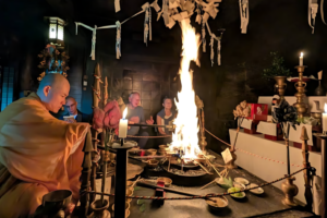 A candid photograph capturing a sacred Japanese Buddhist fire ceremony (Goma) in a dimly lit temple