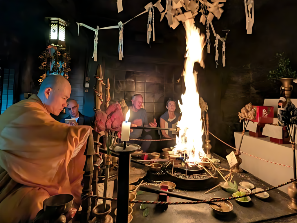 A candid photograph capturing a sacred Japanese Buddhist fire ceremony (Goma) in a dimly lit temple