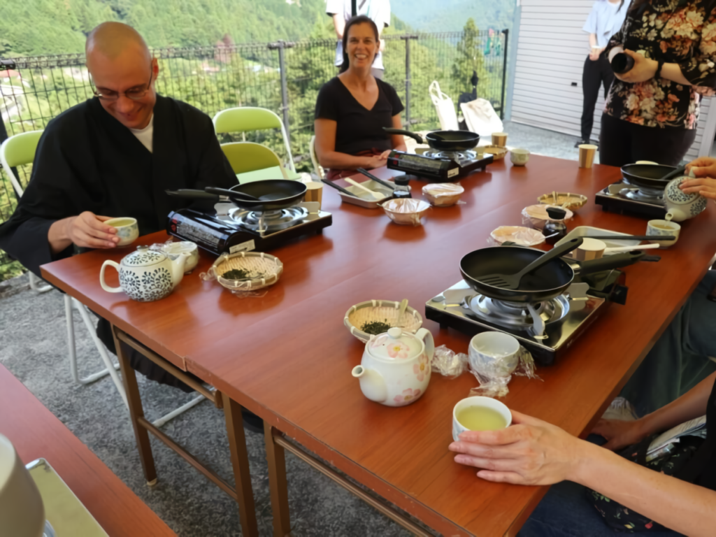 A diverse group enjoys traditional Japanese tea culture on a mountain-view terrace, guided by a monk alongside several women.