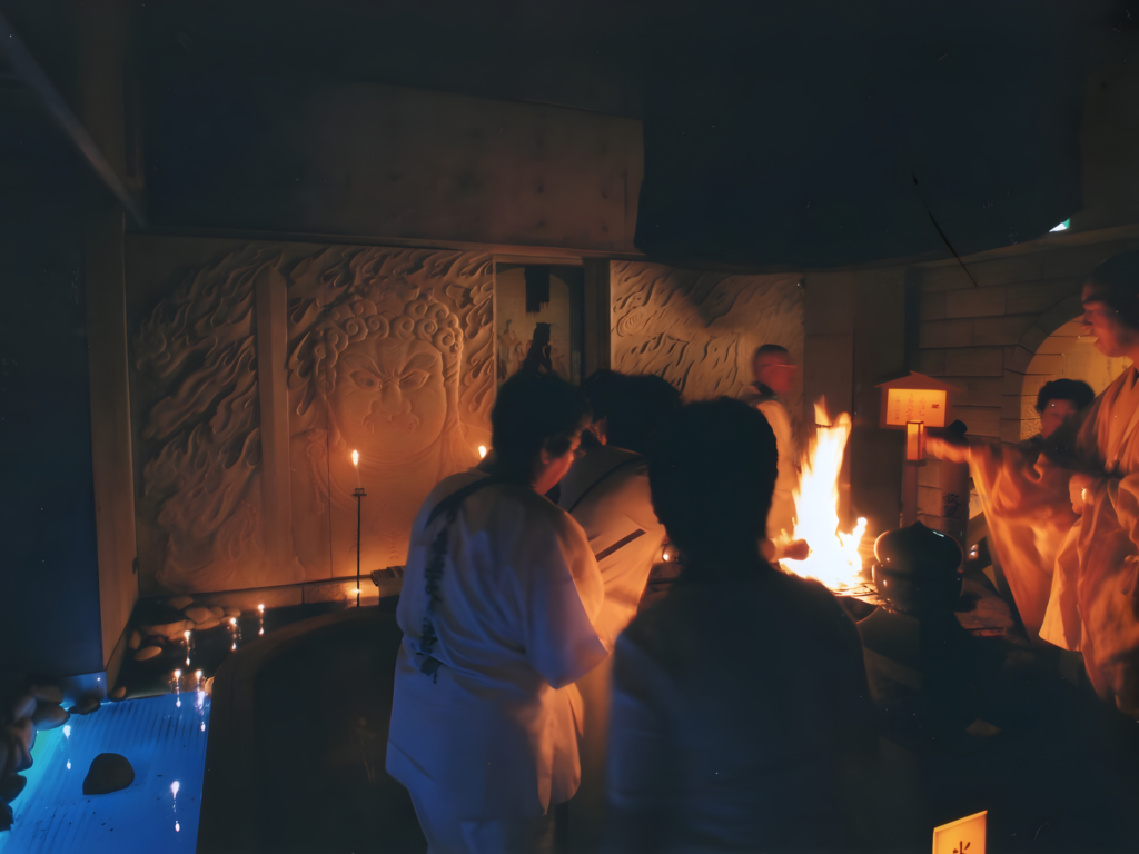A detailed interior view of a dimly lit Japanese Buddhist temple during a traditional Goma fire ritual.