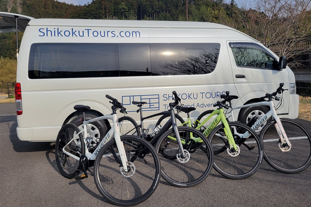 Multiple Specialized bicycles parked in front of a white Shikoku Tours support van in a parking lot.