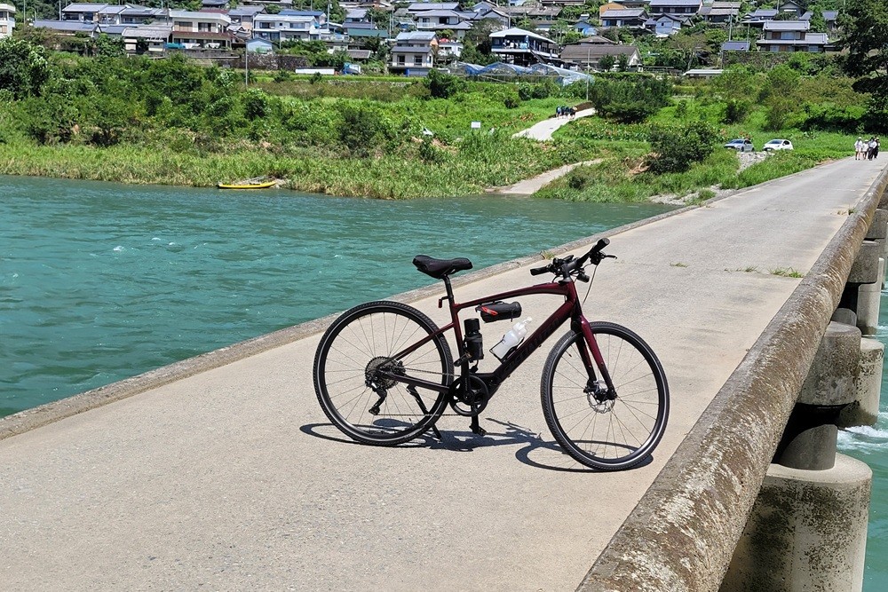 Cycling in Kochi: A bicycle on a traditional low-water bridge with a scenic river and village background.