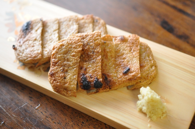 Grilled slices of Ehime's specialty Jakoten fish cakes served with grated ginger on a wooden platter.