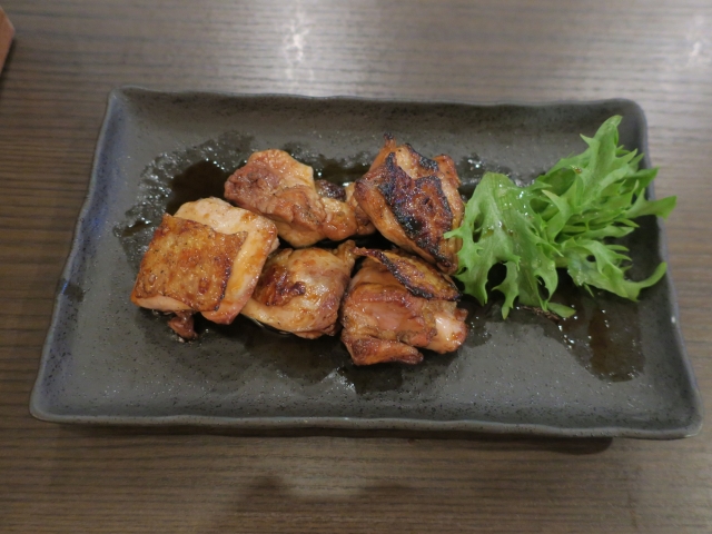 Grilled Awaodori chicken chunks on a black ceramic plate with a side of green lettuce.