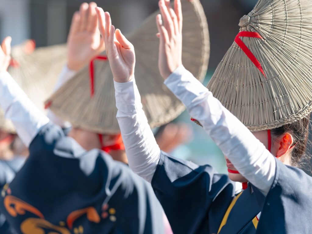 Female Awa Odori dancers in navy yukata and straw amigasa hats raising their hands gracefully mid-dance
