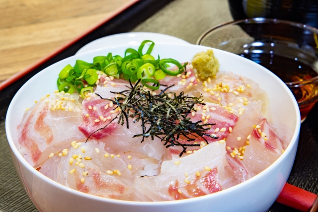 "Uwajima Tai-meshi, a local specialty of Ehime Prefecture: A white bowl filled with rice and covered in fresh raw sea bream sashimi, topped with green onions, nori, and sesame seeds, served with soy sauce on the side.