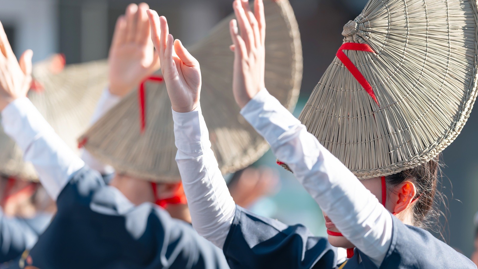 Female Awa Odori dancers in navy yukata and straw amigasa hats raising their hands gracefully mid-dance