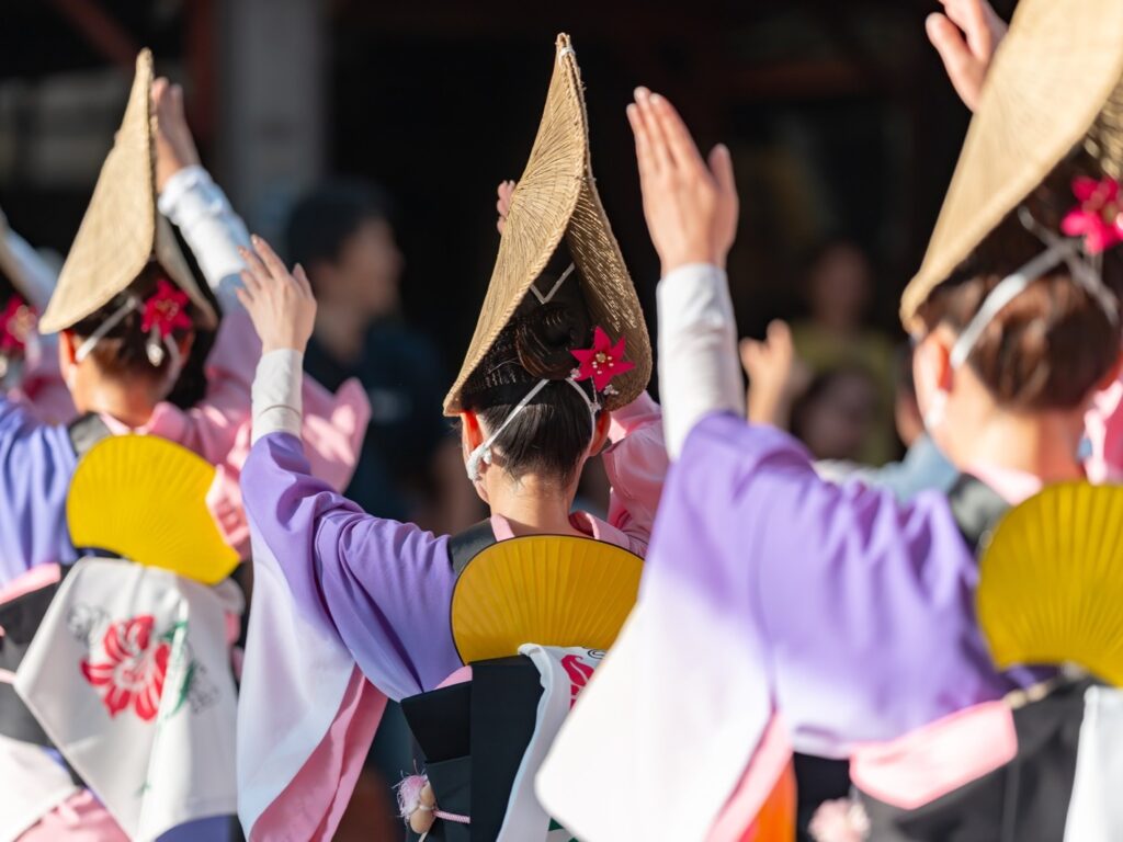 Onna-odori female dancers in purple and pink kimono with pointed straw hats and gold fans, viewed from behind