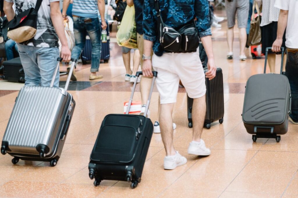 A low-angle view of a crowd of travelers walking on a polished floor, pulling a variety of rolling suitcases, primarily from the waist down.