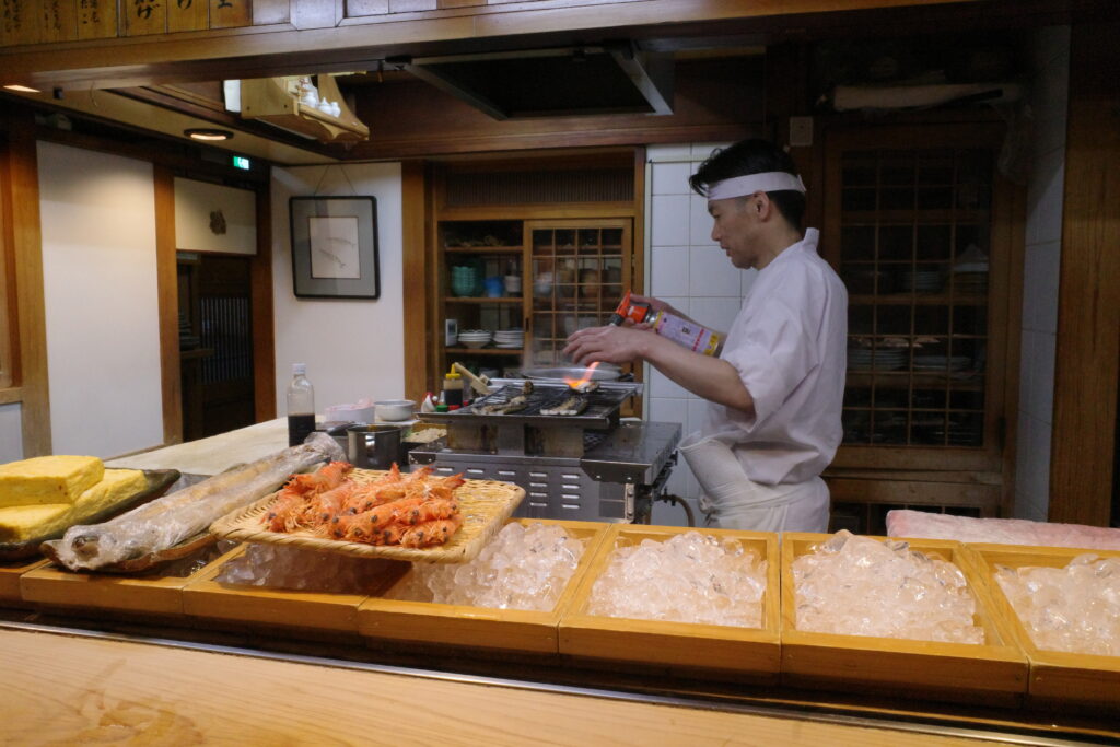 A sushi chef searing ingredients at the counter grill inside the historic Ohira Zushi restaurant in Matsuyama.