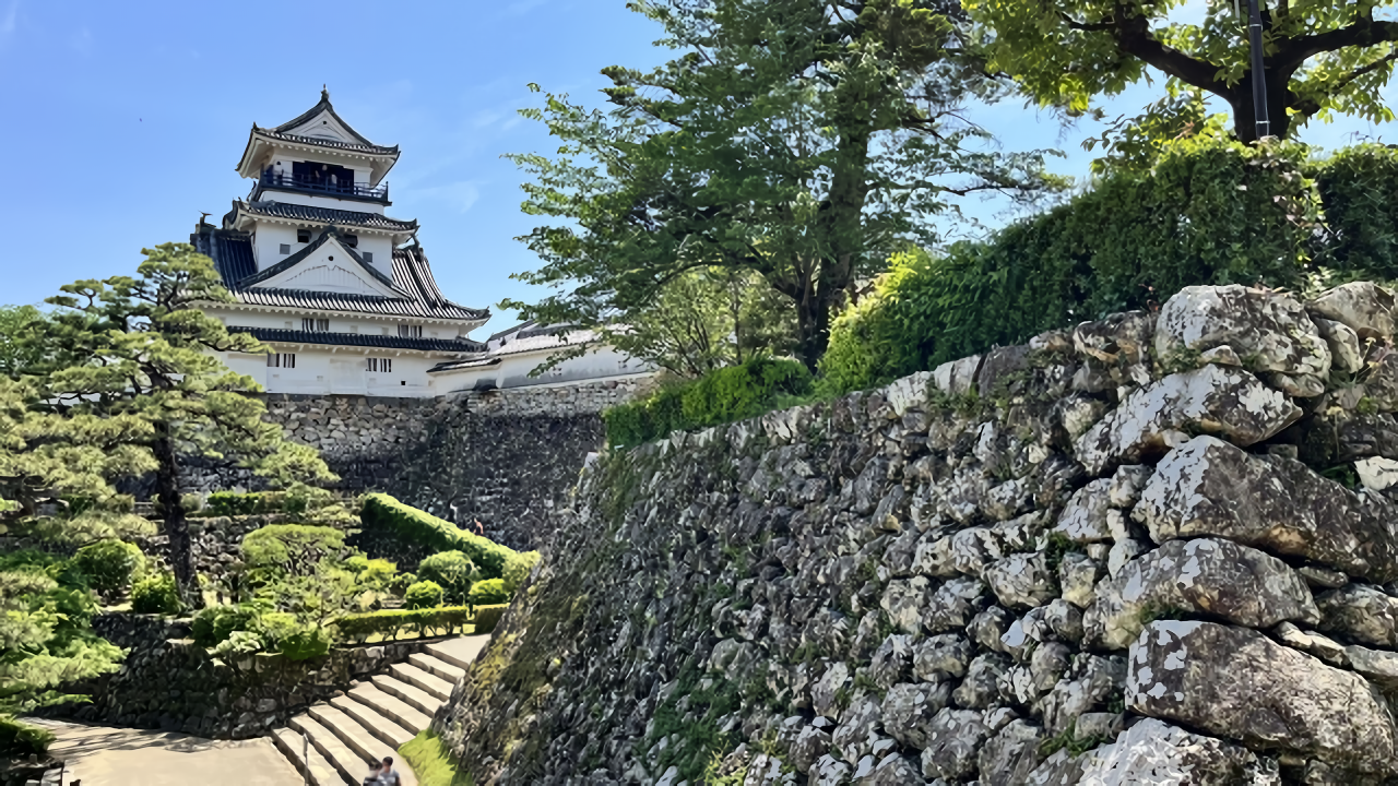 This photo shows the historic Kochi Castle tower standing behind its impressive rugged stone walls under a clear blue sky.