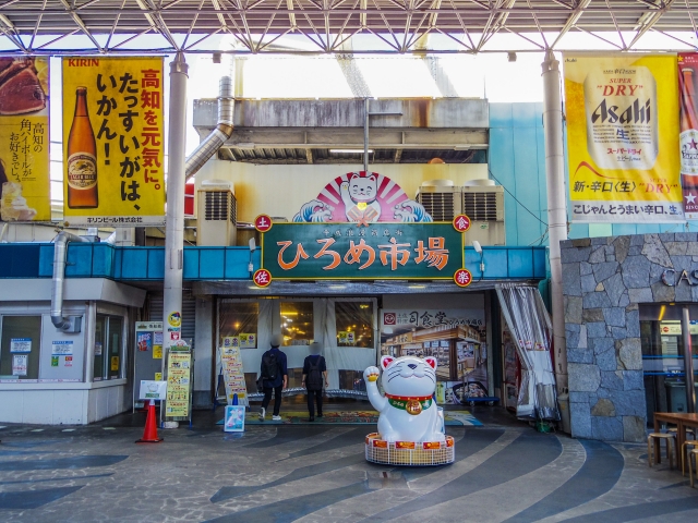 The entrance to Hirome Market in Kochi, featuring a colorful sign and a large beckoning cat statue.