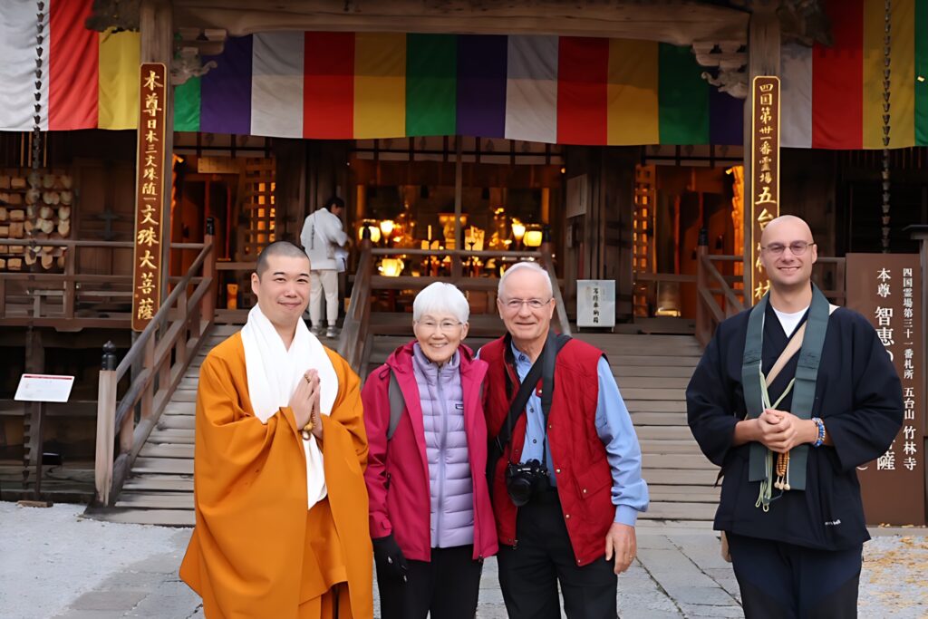 Two Buddhist monks and an elderly tourist couple pose together for a friendly photo in front of Japan's Chikurinji Temple.
