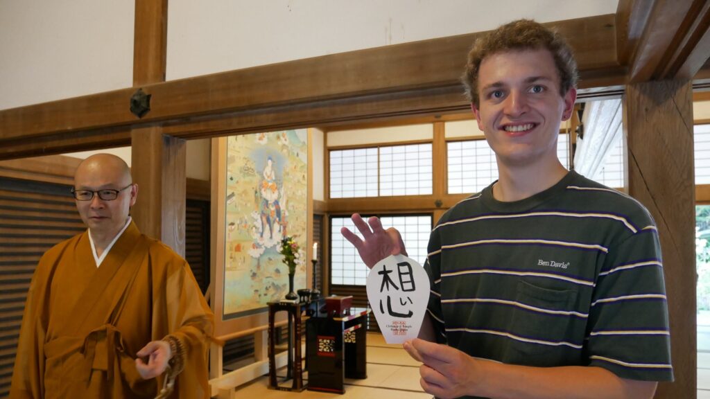 A participant proudly holds a character he's calligraphied next to the temple's head priest.