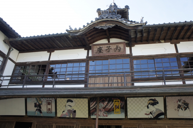 A close-up of the facade highlights the wooden "Uchikoza" nameplate and colorful traditional paintings illustrating classical Japanese performances below the eaves.