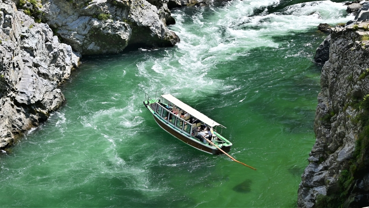 A sightseeing boat glides through Oboke Gorge, winding between dramatic rock cliffs along the emerald-green waters of the Yoshino River.