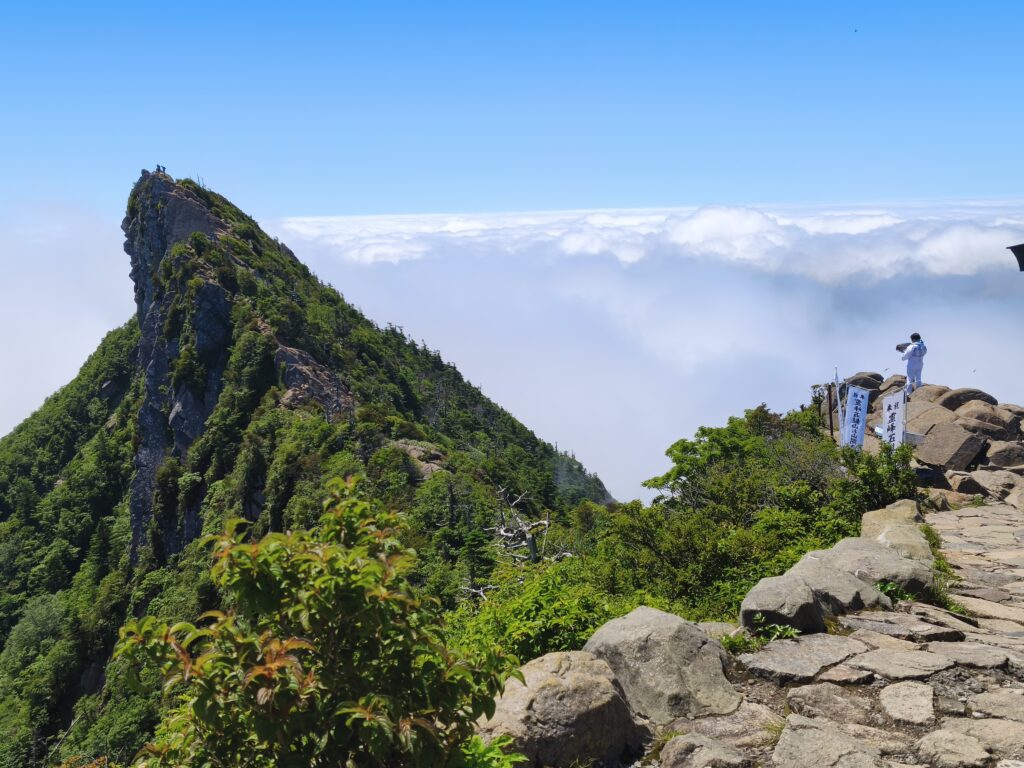 A white-clad pilgrim looks toward the rocky peak of Mt. Ishizuchi juts above a sea of clouds.