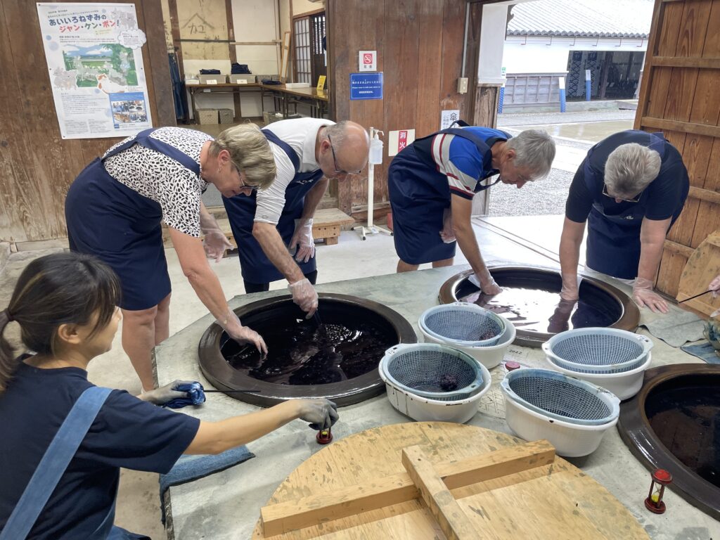 Visitors immerse fabric in indigo vats under the guidance of a craftswoman at Ai no Yakata.