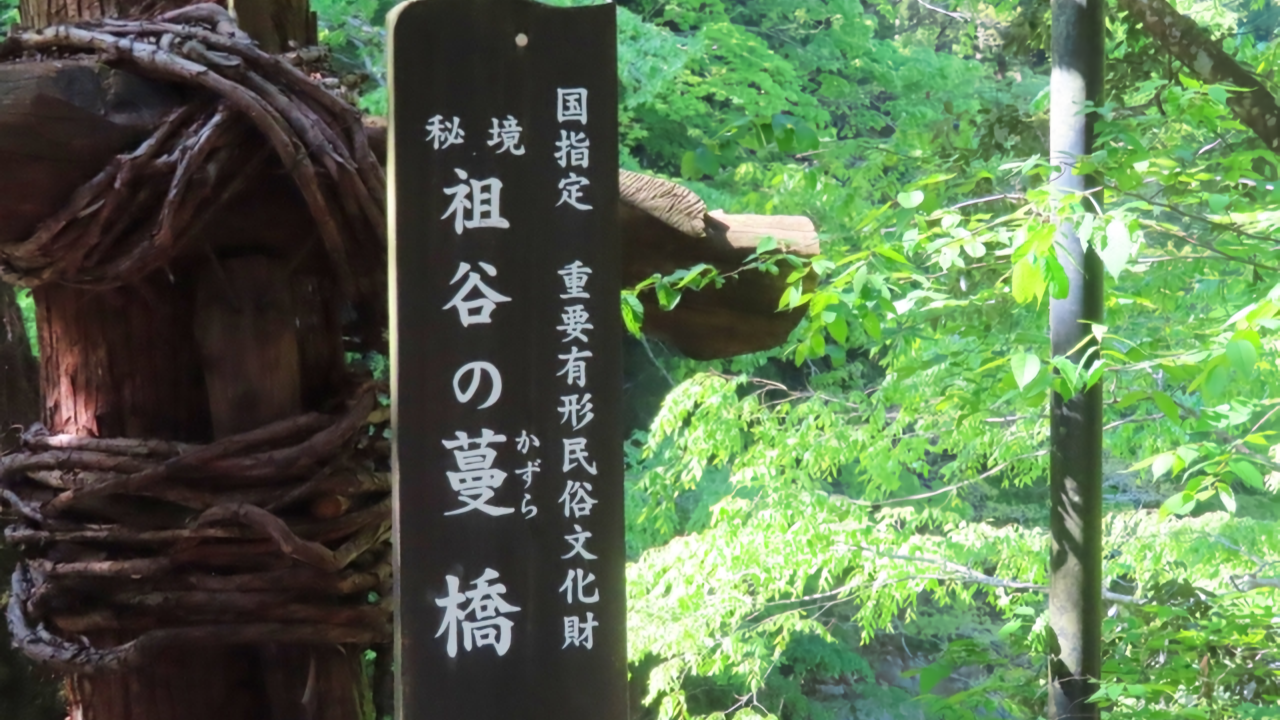 A wooden sign marks the Iya Valley Kazura Bridge, a nationally designated Important Tangible Folk Cultural Property, framed by the lush forest of this hidden region.