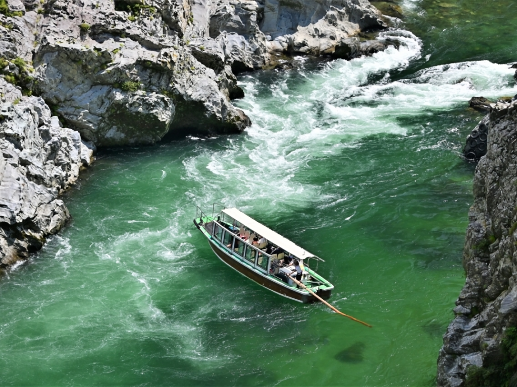 A sightseeing boat glides through Oboke Gorge, winding between dramatic rock cliffs along the emerald-green waters of the Yoshino River.