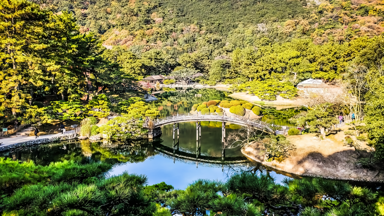 A sweeping panorama showcases the arched bridge, mirror-like pond, sculpted pines, and golden-tinged hillside in warm afternoon light.
