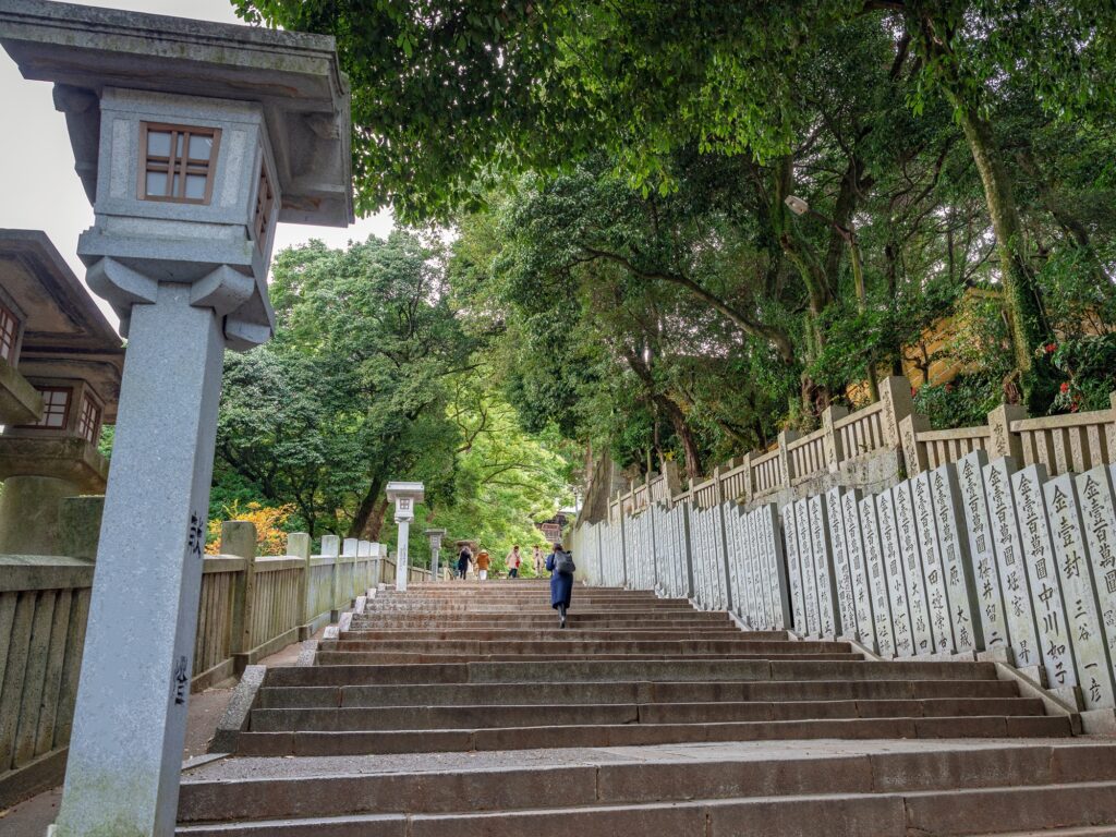 Rows of inscribed donation pillars line the climb, each stone recording a gift to the shrine — a thousand years of gratitude, carved and standing.