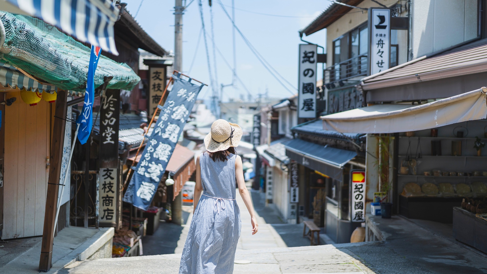 The shop-lined approach to Konpira-san, where worn stone paving, hand-painted banners, and souvenir stalls greet pilgrims long before the first step.