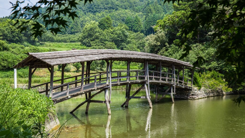 A roofed wooden bridge arches across a still pond to Yuge Shrine, one of Uchiko's most peaceful spots and an easy bike ride away.