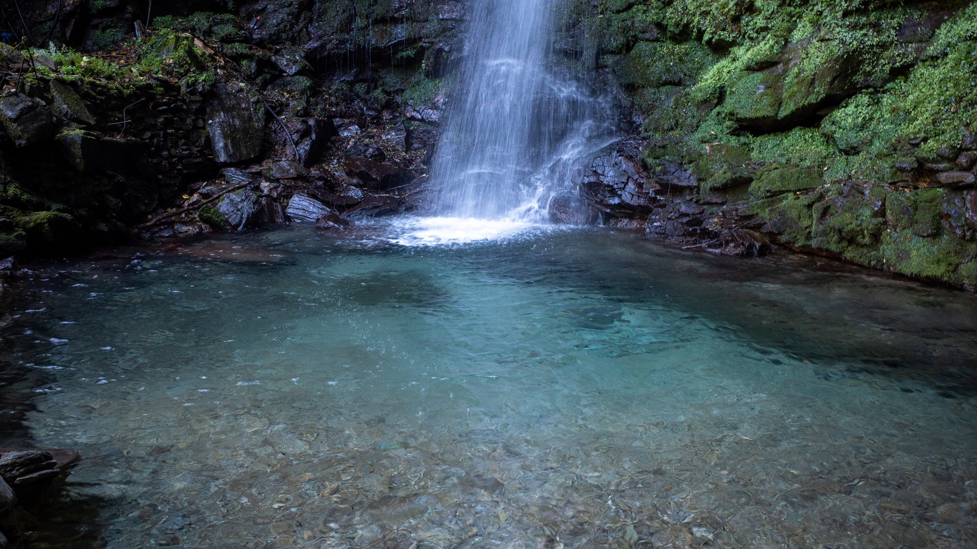 A single column of water dropping into the clear emerald plunge pool below Biwa Falls
