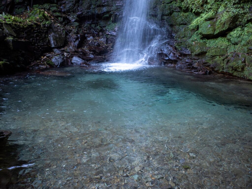 A single column of water dropping into the clear emerald plunge pool below Biwa Falls
