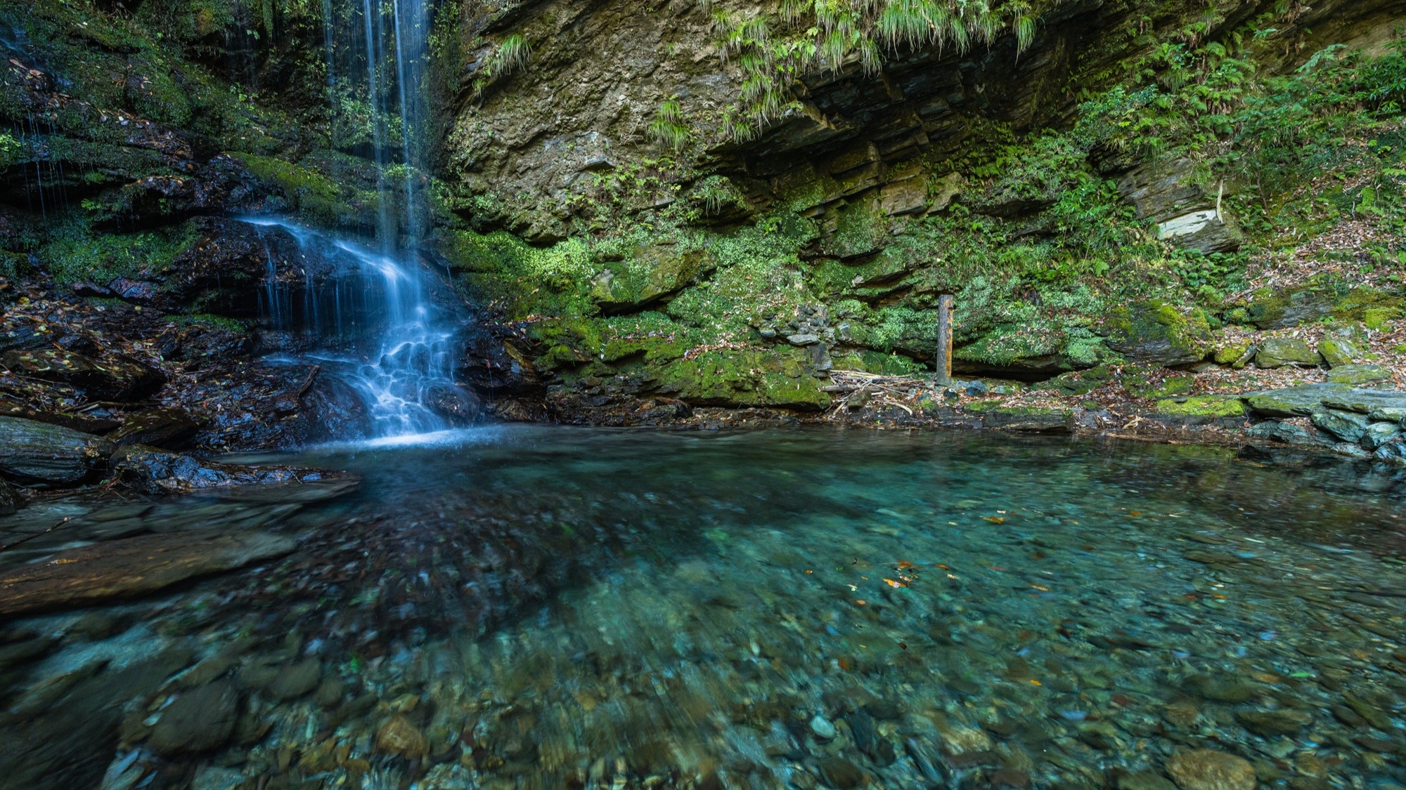Wide view of Biwa Falls and its clear pool, with river stones visible through the water, Iya Valley