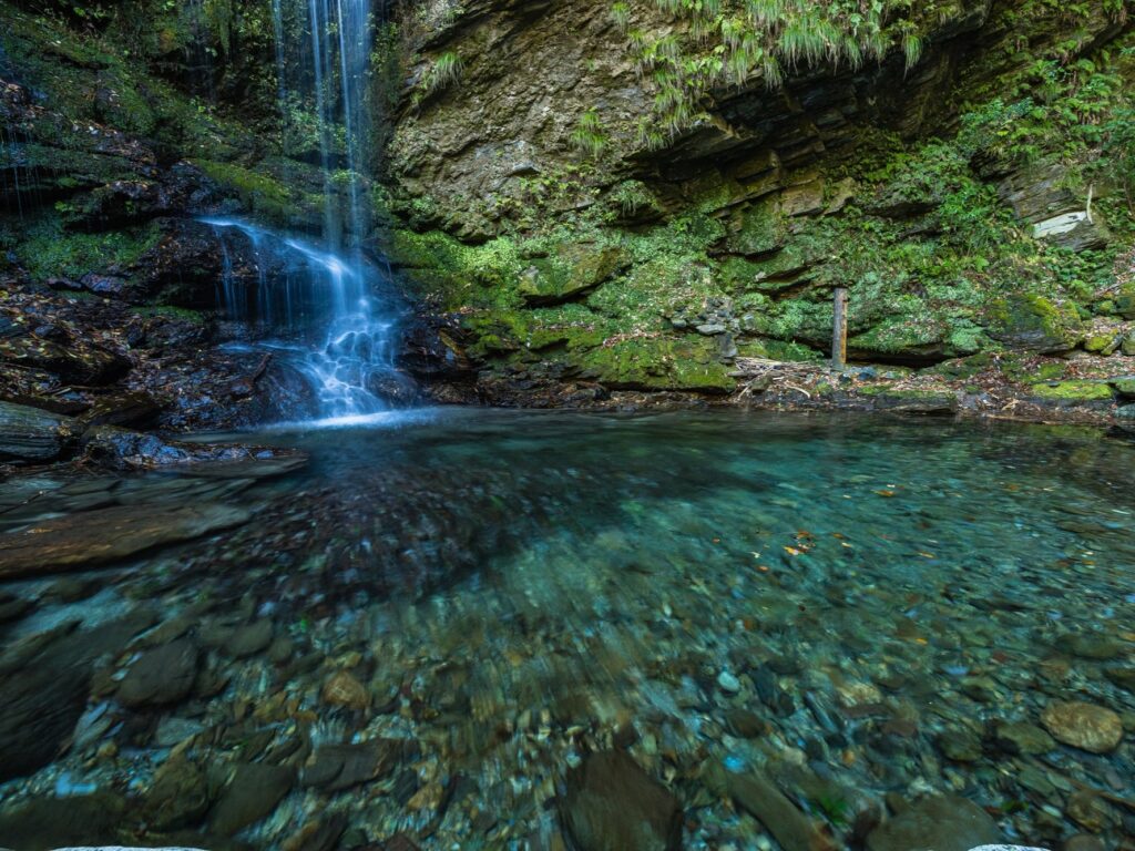 Wide view of Biwa Falls and its clear pool, with river stones visible through the water, Iya Valley