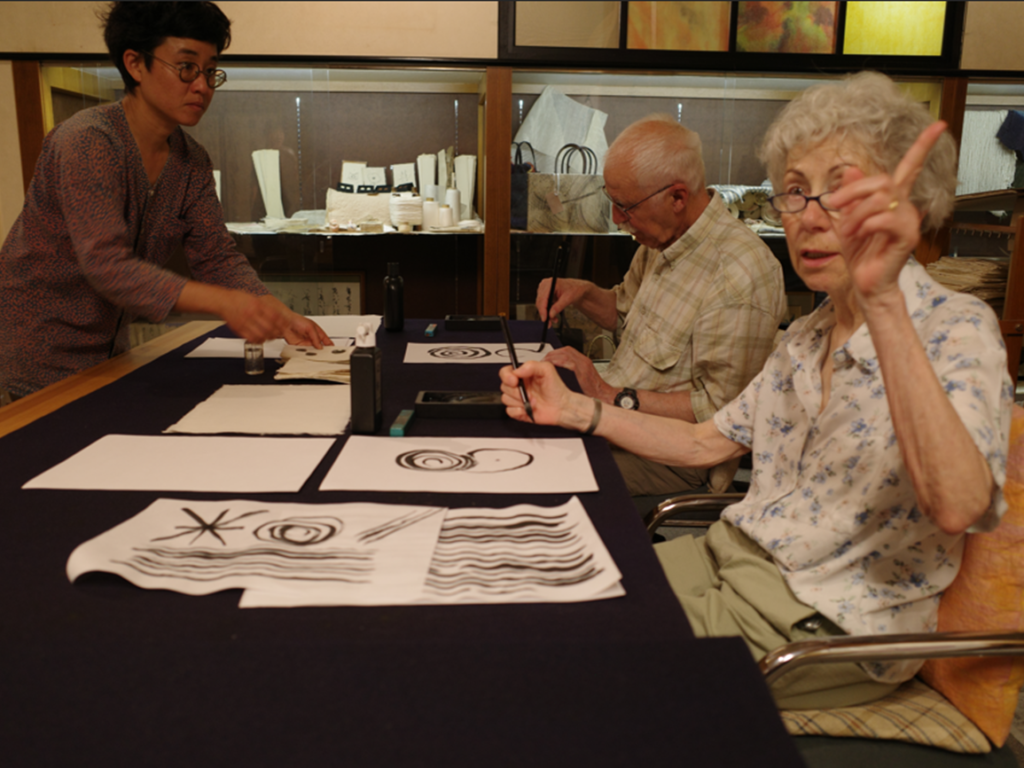 Guests practicing Japanese calligraphy on handmade washi paper with an instructor