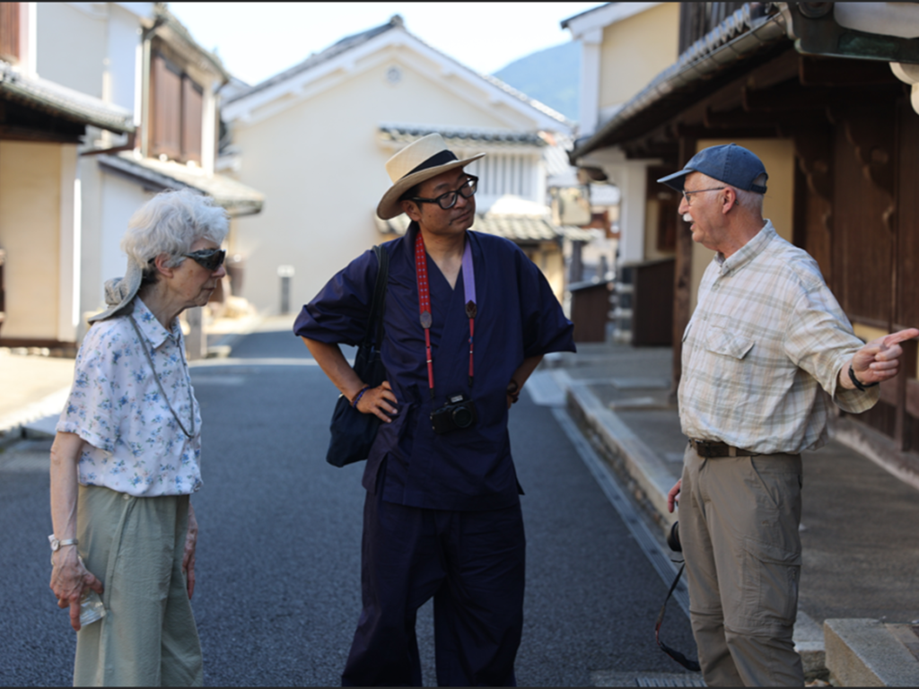 Local guide in samue talking with guests along the historic white-walled streets of Uchiko, Ehime