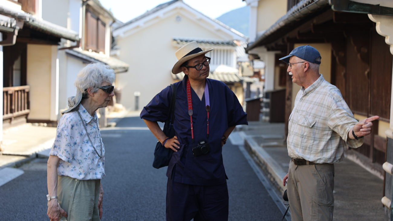 Local guide in samue talking with guests along the historic white-walled streets of Uchiko, Ehime