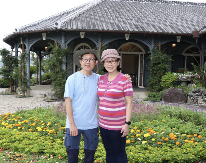 Two smiling Travellers in sun hats standing together in front of a colorful flower garden
