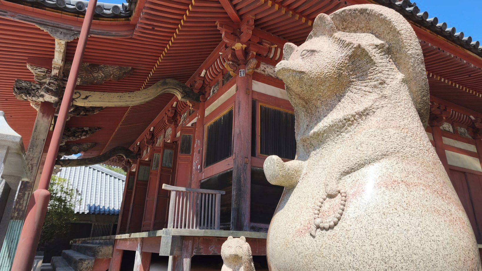 Two stone Tanuki stand guard in front of the vermillion hall of Yashima-ji Temple.