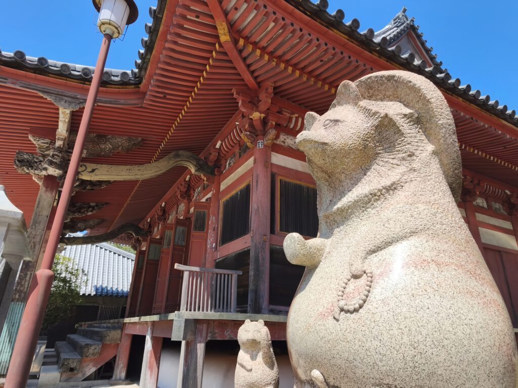 Two stone Tanuki stand guard in front of the vermillion hall of Yashima-ji Temple.
