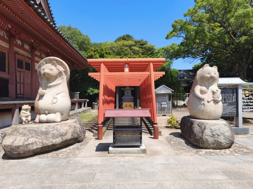 A family of Tanuki guard a series of red torii gates leading to a small Shintō Shrine in the grounds of Yashima-ji Temple