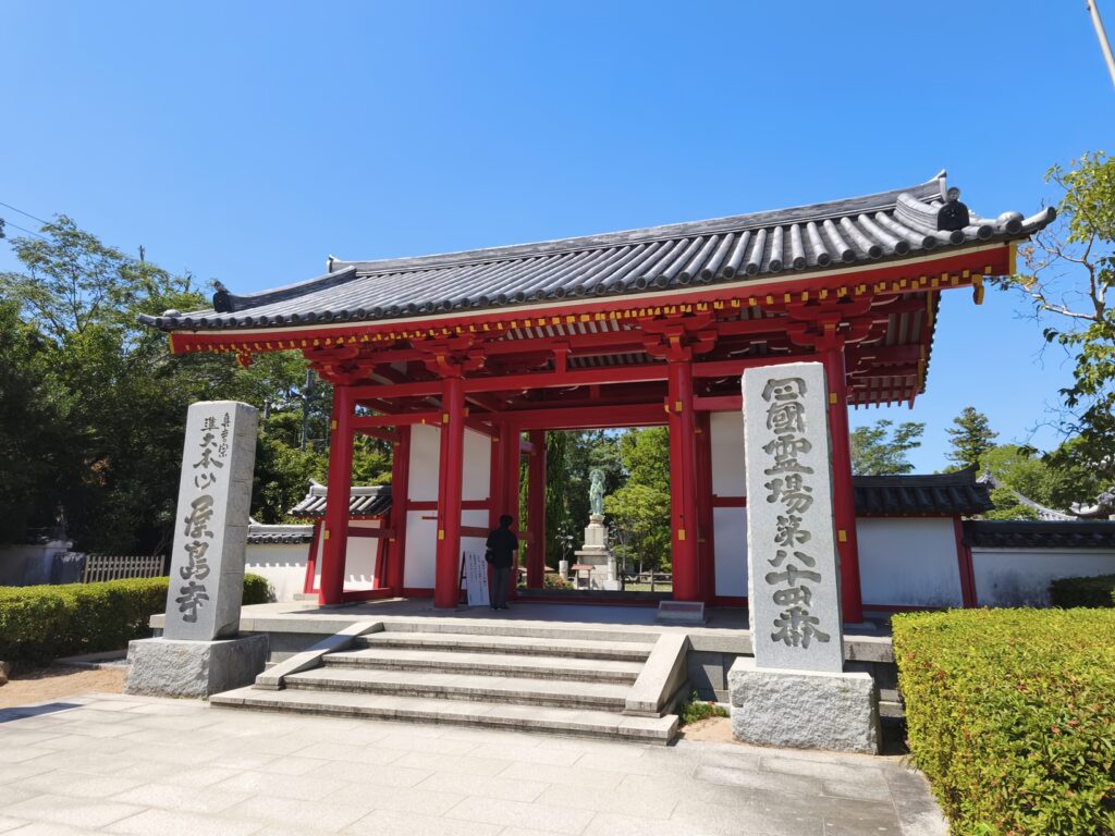 The vermillion gate of Yashima-ji Temple, with stone markers reading "Yashima-ji" and "Shikoku Pilgrimage Temple Number 84" in Chinese characters