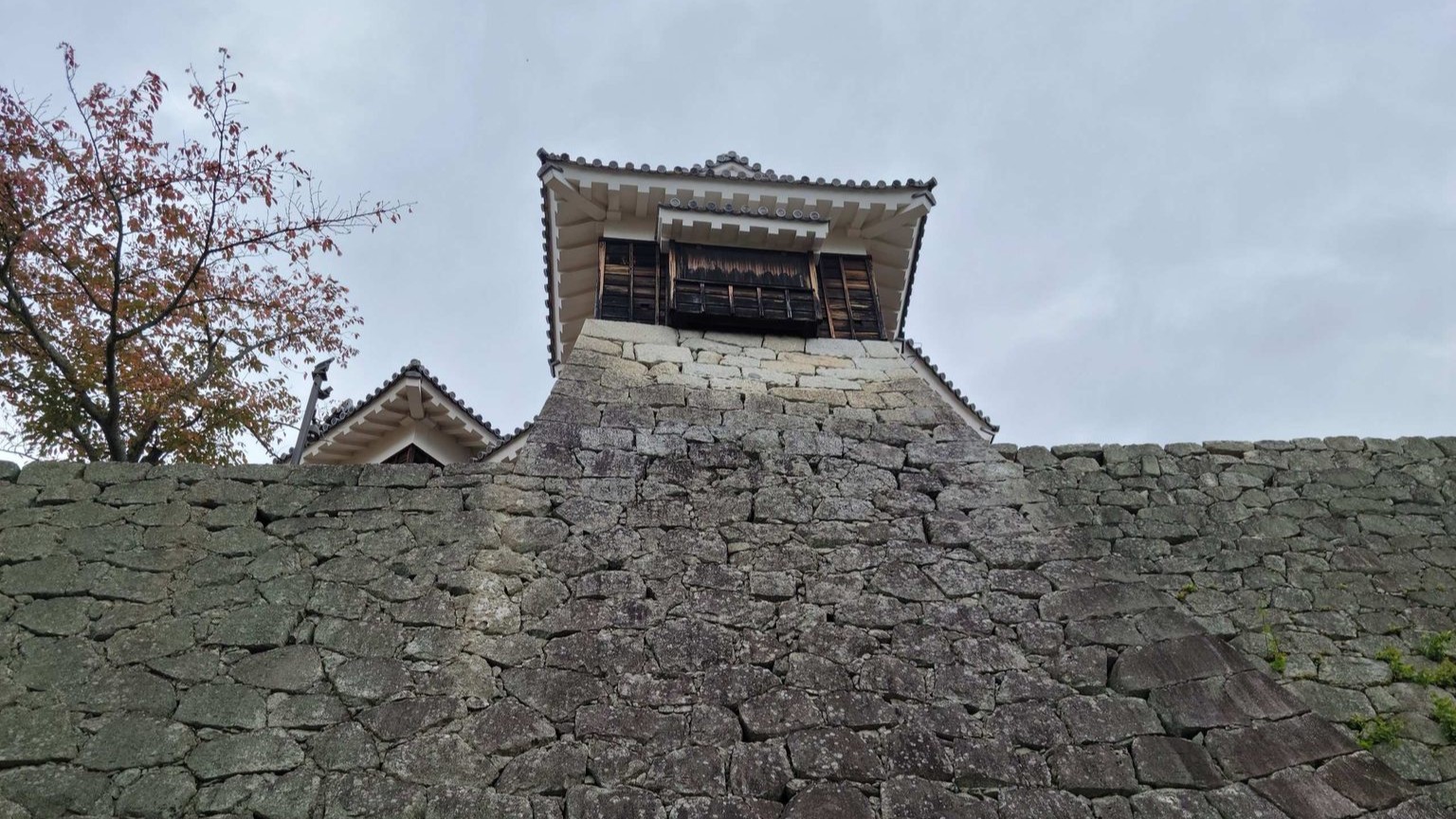 A wooden tower stands atop the a stone wall of Matsuyama Castle.