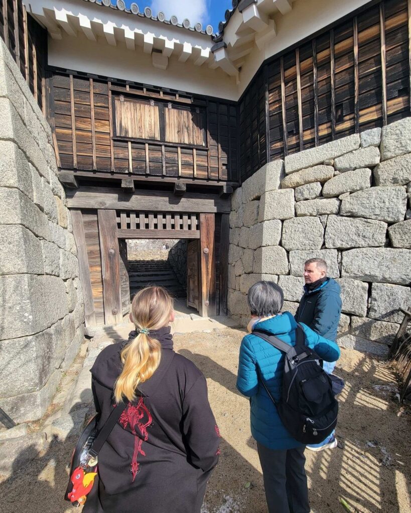 Visitors approach one of the gates of Matsuyama Castle. Atop the stone walls, wooden buildings are studded with portholes that would allow defenders to rain death on attackers.