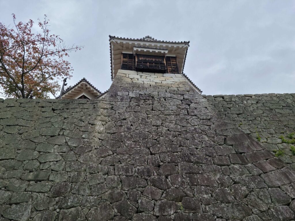 A wooden tower stands atop the a stone wall of Matsuyama Castle.