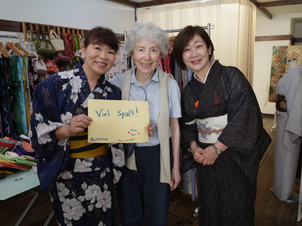 Guest with kimono dressing staff holding a handwritten welcome sign after a yukata dressing experience in Matsuyama