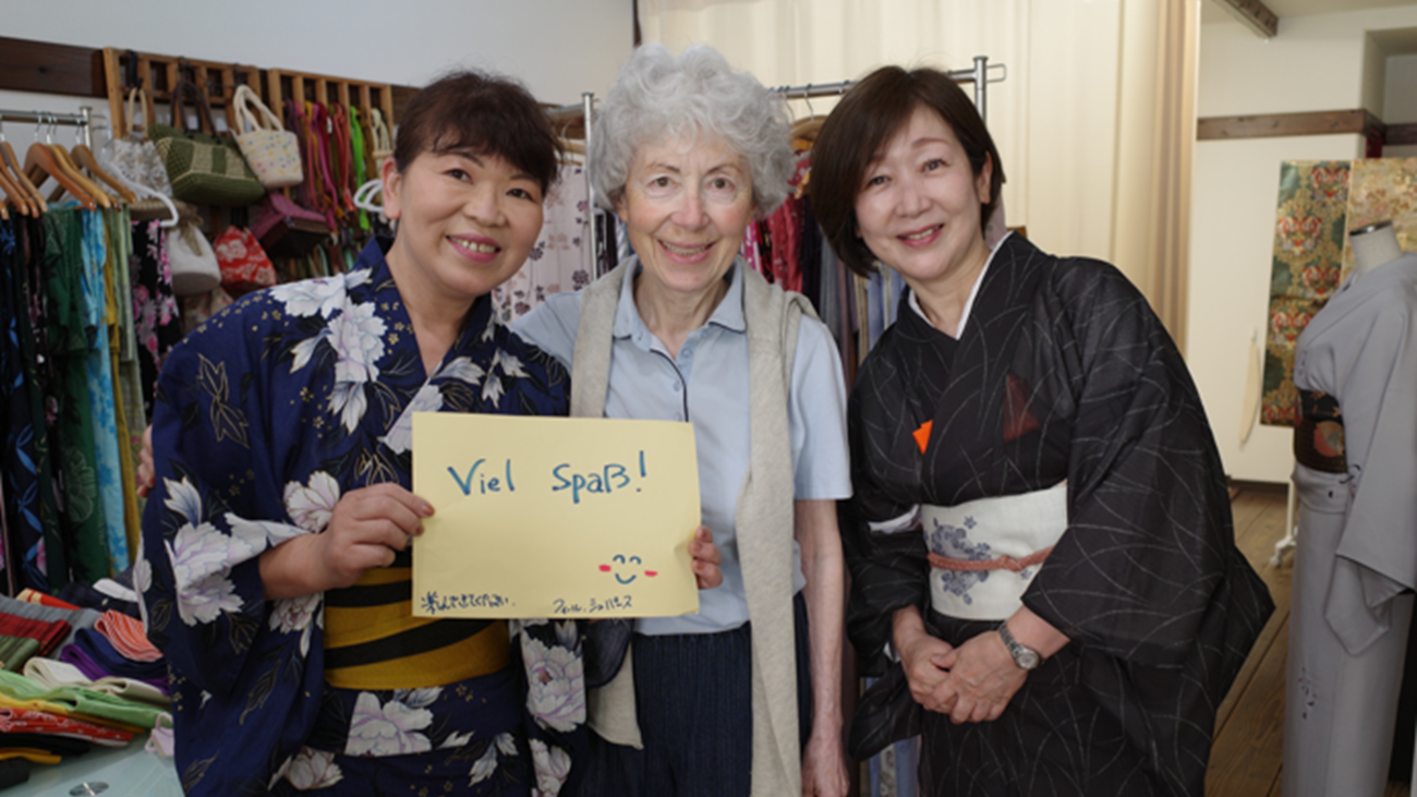 Guest with kimono dressing staff holding a handwritten welcome sign after a yukata dressing experience in Matsuyama